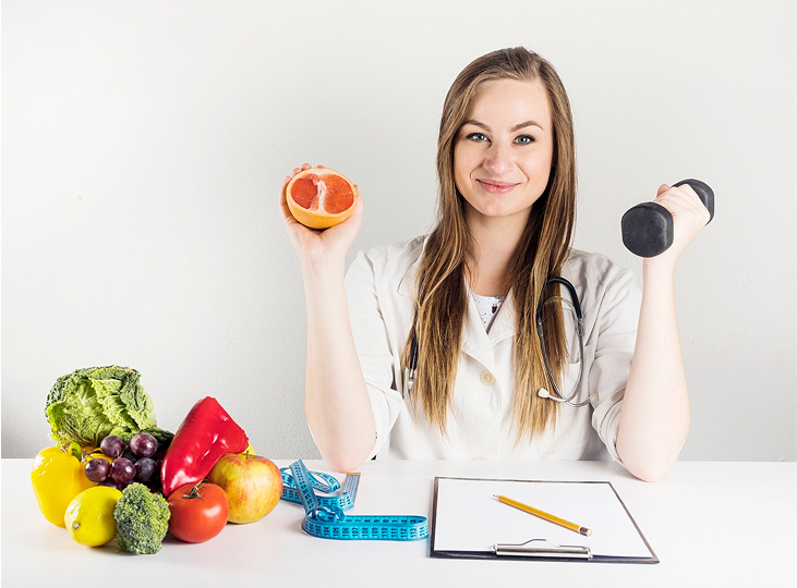 Female dietician holding grapefruit and dumbbell in clinic